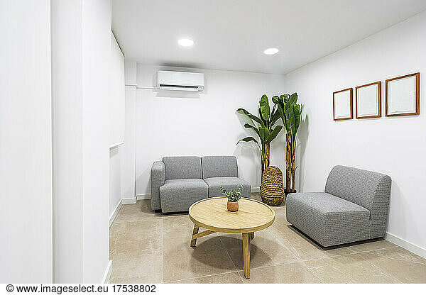 Table and sofa arranged in illuminated waiting room at clinic