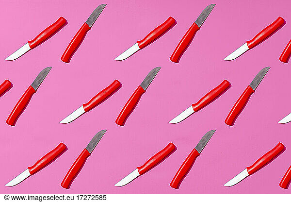 Table knives arranged on pink background