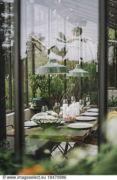 Table setup for dinner party in back yard greenhouse seen through glass window