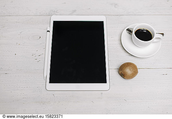 Tablet  cup of coffee and kiwi on wooden surface