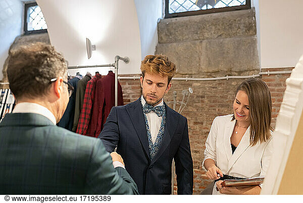 Tailor fitting suit on client near assistant