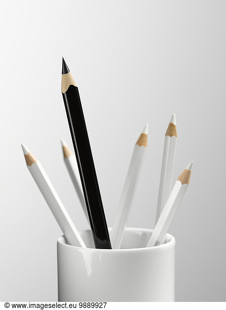 Tall black pencil in cup with smaller white pencils still life