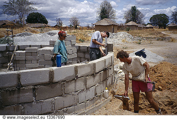 TANZANIA Work Men laying building blocks for a water tank in a small village with thatched huts