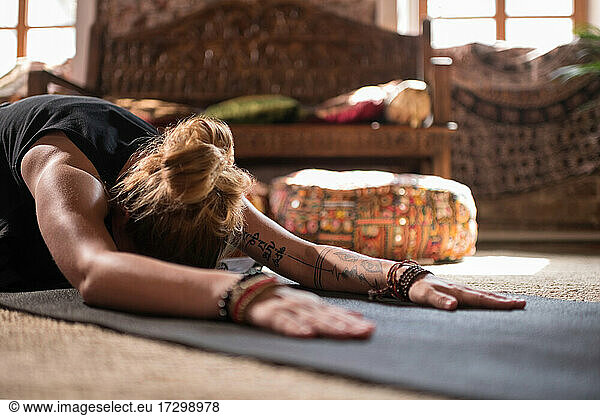 Tattooed female stretching in Utthita Balasana pose