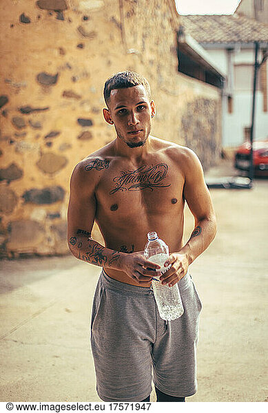 Tattooed latin guy without a shirt drinking water after training