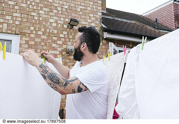 Tattooed man drying sheet on clothesline at back yard