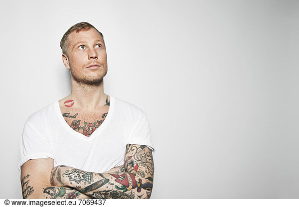 Tattooed man with arms crossed looking away against grey background