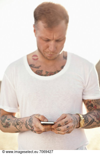 Tattooed mid adult man with text messaging outdoors