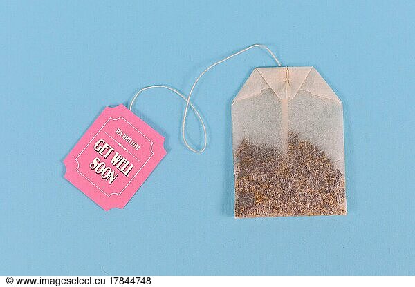 Tea bag with made up cute pink label with text Get well soon on pastel blue background