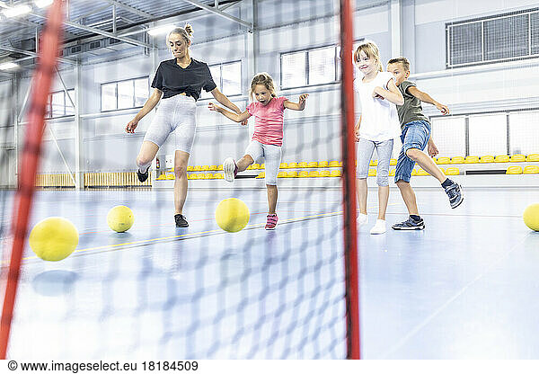 Teacher and students kicking ball in net at school sports court