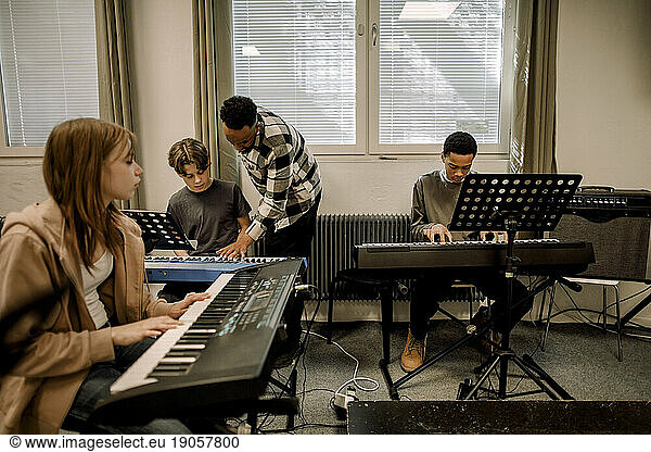 Teacher assisting teenage students during piano class at high school