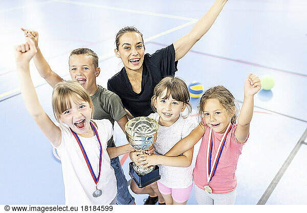 Teacher celebrating victory with students holding trophy at school sports court