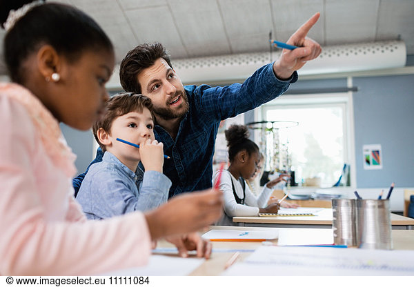 Teacher discussing with boy while pointing in classroom at school