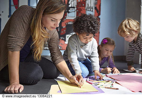 Teacher drawing on papers with students at preschool