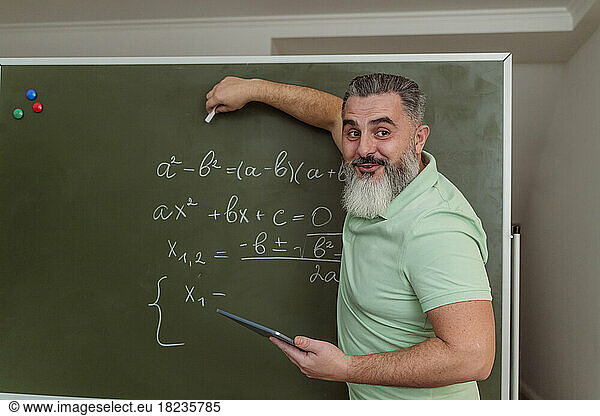 Teacher explaining mathematics on chalkboard holding tablet PC