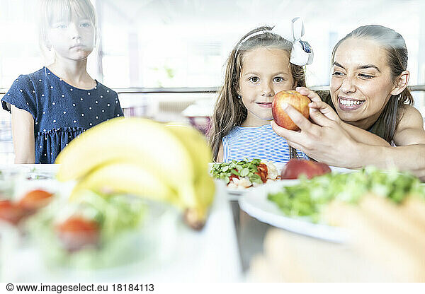 Teacher giving apple to student in school cafeteria