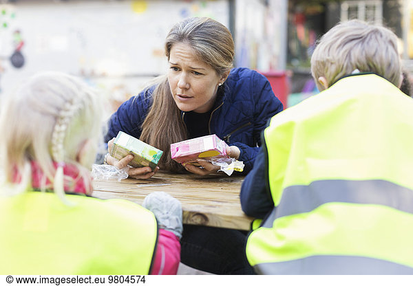 Teacher holding juice boxes while communicating with children outside kindergarten