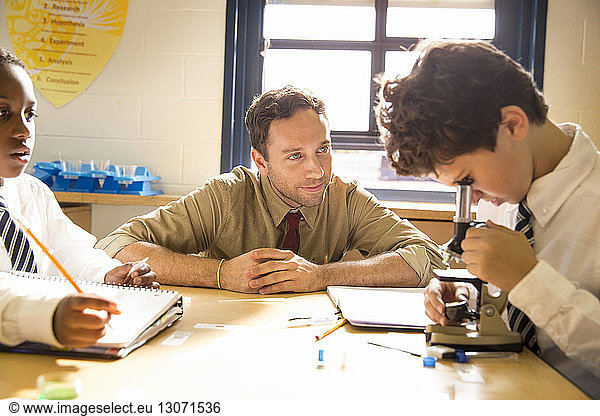 Teacher looking at schoolboy practicing science experiment