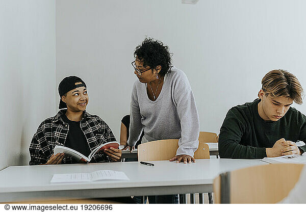 Teacher looking at smiling male student sitting in classroom