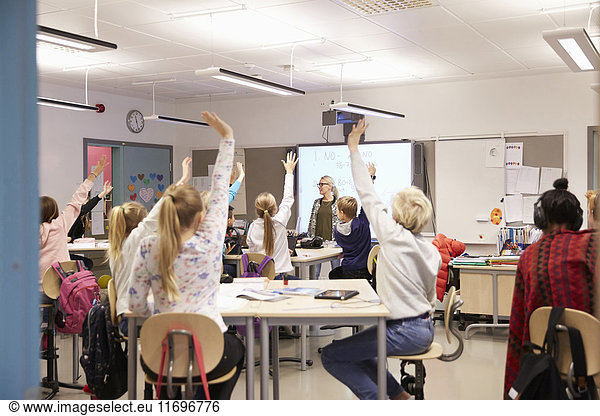 Teacher looking at students with arms raised in classroom