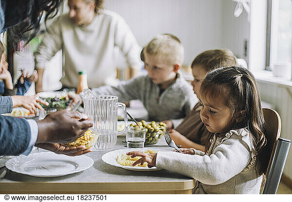 Teacher serving food to male and female students for breakfast in day care center