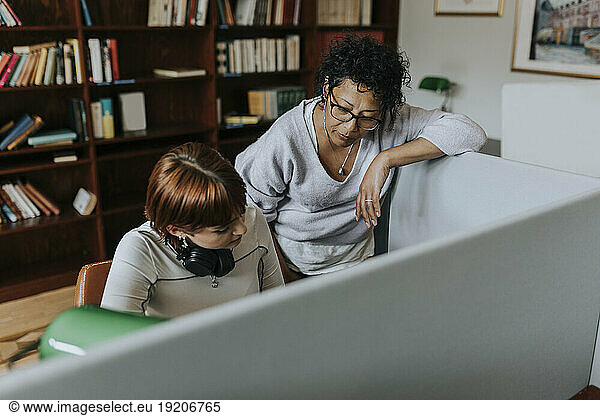 Teacher standing by female teenage student in library