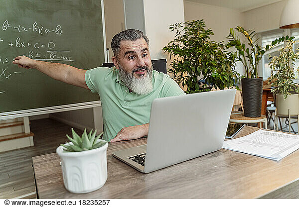 Teacher taking online lecture through video call on laptop at desk