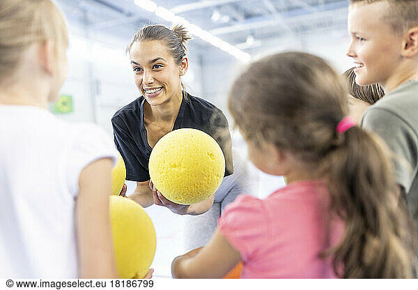 Teacher talking to students holding ball at school sports court