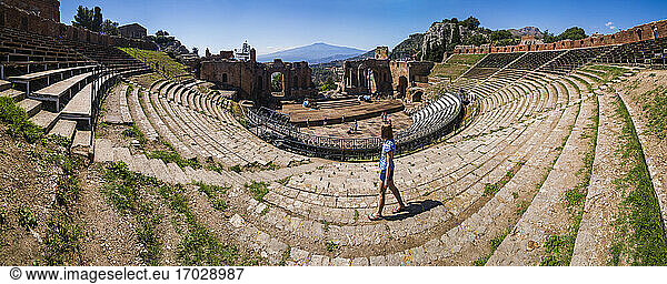 Teatro Greco alias Taormina Griechisches Theater  Panoramafoto von Touristen Sightseeing im Amphitheater mit Vulkan Ätna im Hintergrund  Sizilien  Italien  Europa. Dies ist ein Panoramafoto von einem Touristen Sightseeing am Teatro Greco alias Taormina Griechisches Theater oder Amphitheater  mit dem Vulkan Ätna im Hintergrund  Sizilien  Italien  Europa. Beim Sightseeing ist dies eines der besten Dinge  die man als Tourist in Taormina tun kann  dank seiner atemberaubenden Lage mit Panoramablick auf den Ätna.