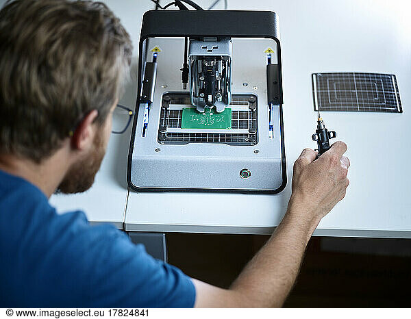 Technician looking at milling machine cutting circuit board in electronic laboratory