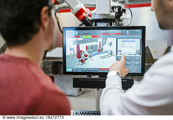 Technician pointing on computer screen with colleague at robot factory