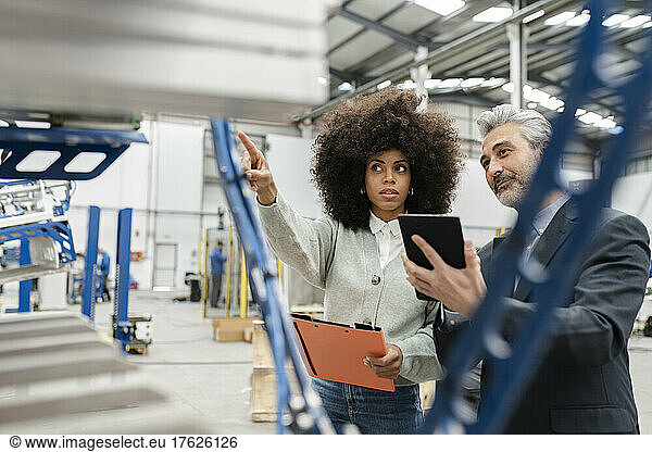 Technician showing machine to businessman with tablet PC in factory