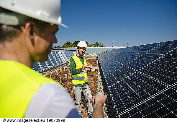 Technician talking to colleague on the roof of a company building with solar panels