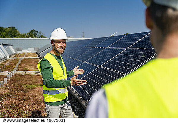Technician talking to colleague on the roof of a company building with solar panels