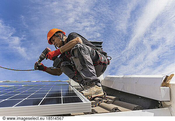 Technician using drill machine and installing solar panels on roof