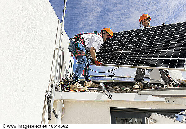 Technician with colleague installing solar panel on roof