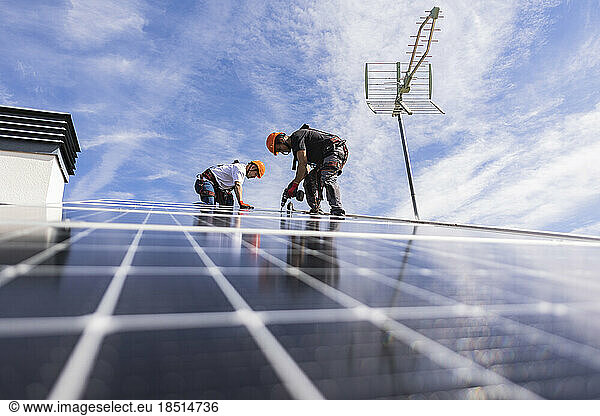 Technician with colleague using drill on solar panel