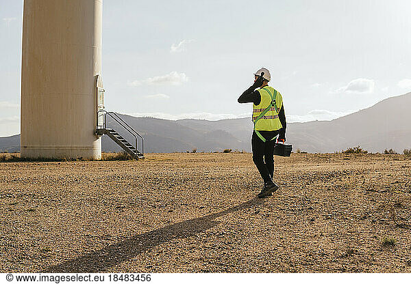 Technician with toolbox walking towards wind turbine