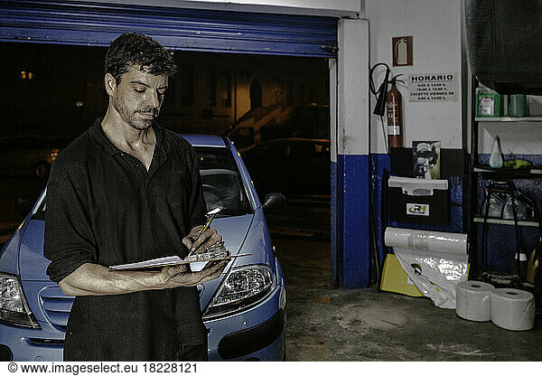 Technician writing on clipboard near car in garage