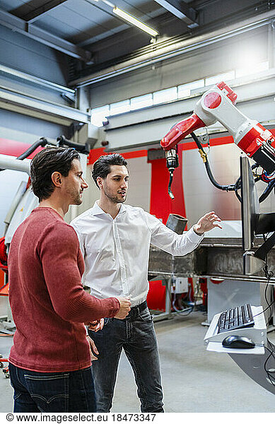 Technicians discussing over robotic arm at industry