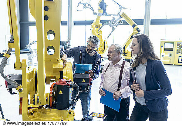 Technicians examining industrial robot in factory