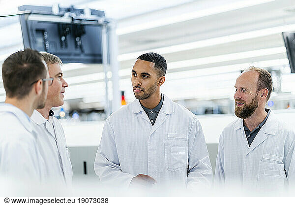 Technicians in lab coats discussing in electronics factory