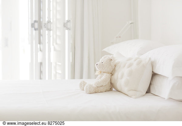 Teddybär und Kissen auf weißem Bett