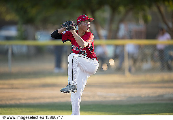 teen baseball pitcher in red uniform in full wind up on the mound