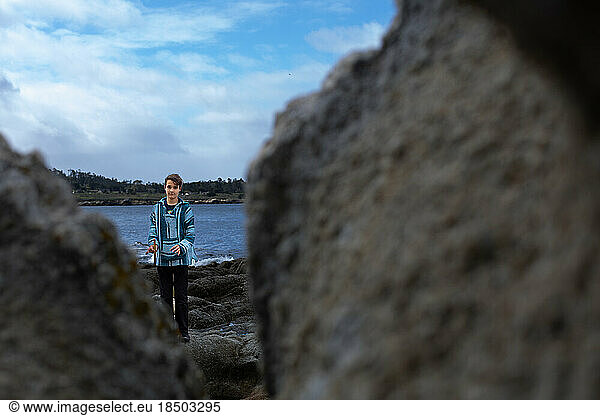 Teen Boy At The Coast Holding Sticks Framed By Boulders