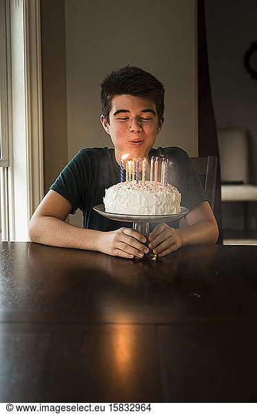 Teen boy blowing out the candles on his birthday cake at the table.