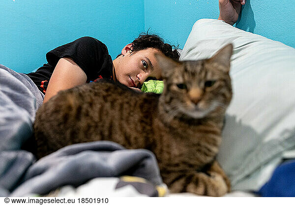 Teen boy lays in bed awake with his brown tabby cat