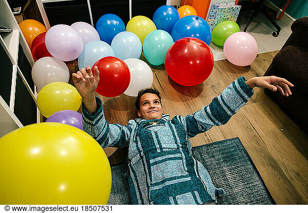 Teen boy lays on the ground surrounded by colorful balloons