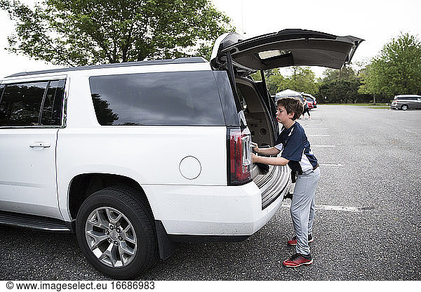 Teen Boy Loads Baseball Equipment Into Rear of White SUV After Game