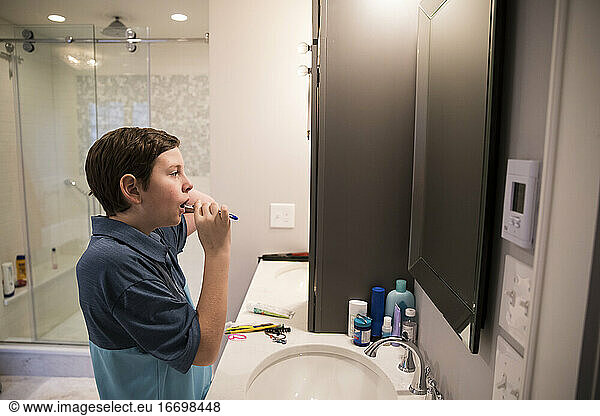 Teen Boy Looks in Mirror While Brushing His Teeth in Modern Bathroom
